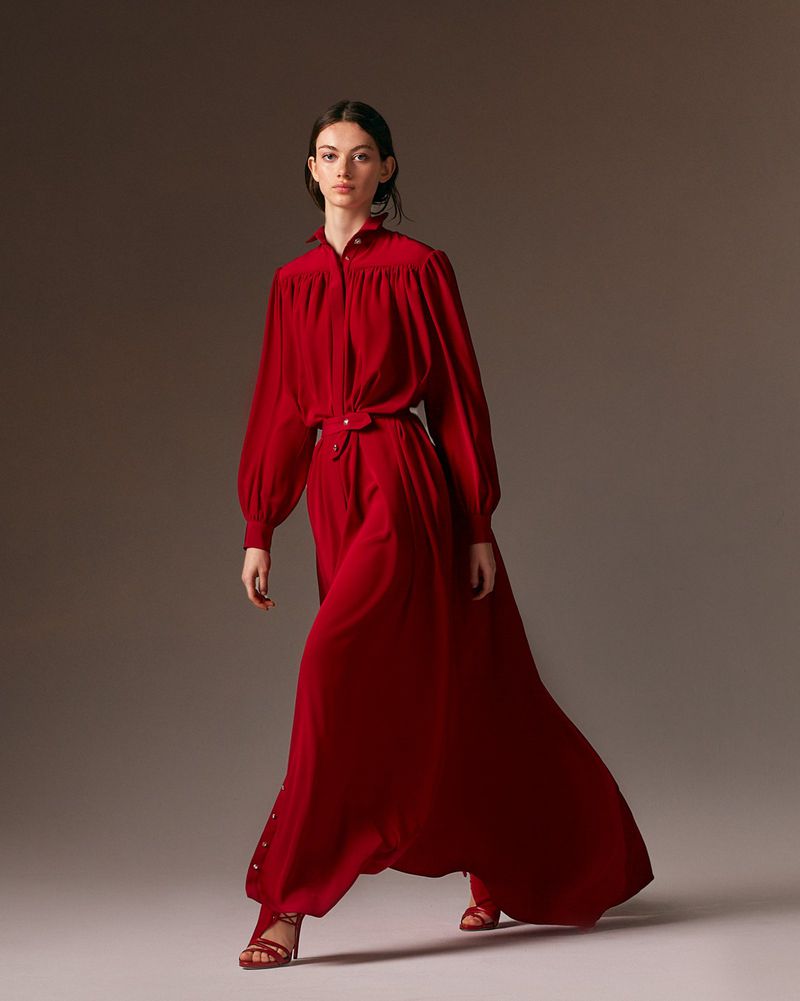 Model Lydia Waldrop wearing a long flowing red gown and strappy red heels against a neutral studio backdrop for Alexis Mabille.