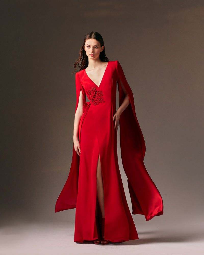 Elegant woman in a flowing red gown with a V-neck and side slit, posing in a studio with soft lighting and a neutral background.