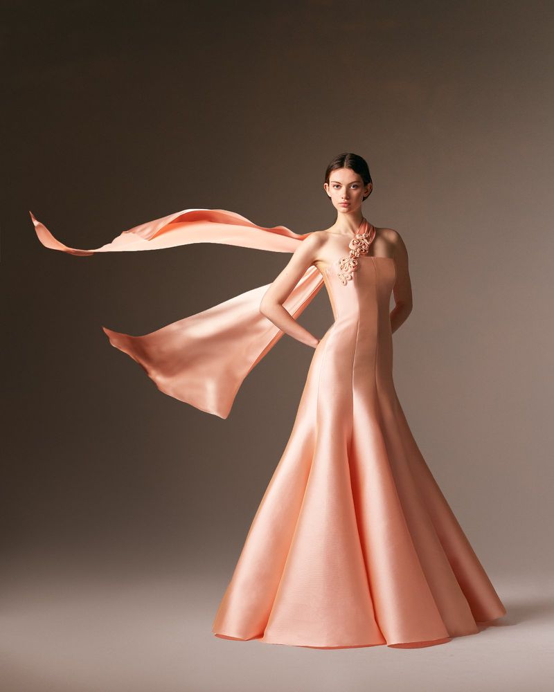 Elegant woman posing in a peach satin gown with flowing scarf, studio shot, capturing fashion and beauty in a sophisticated setting.