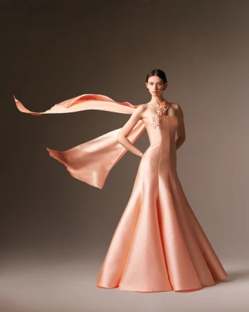 Elegant woman posing in a peach satin gown with flowing scarf, studio shot, capturing fashion and beauty in a sophisticated setting.