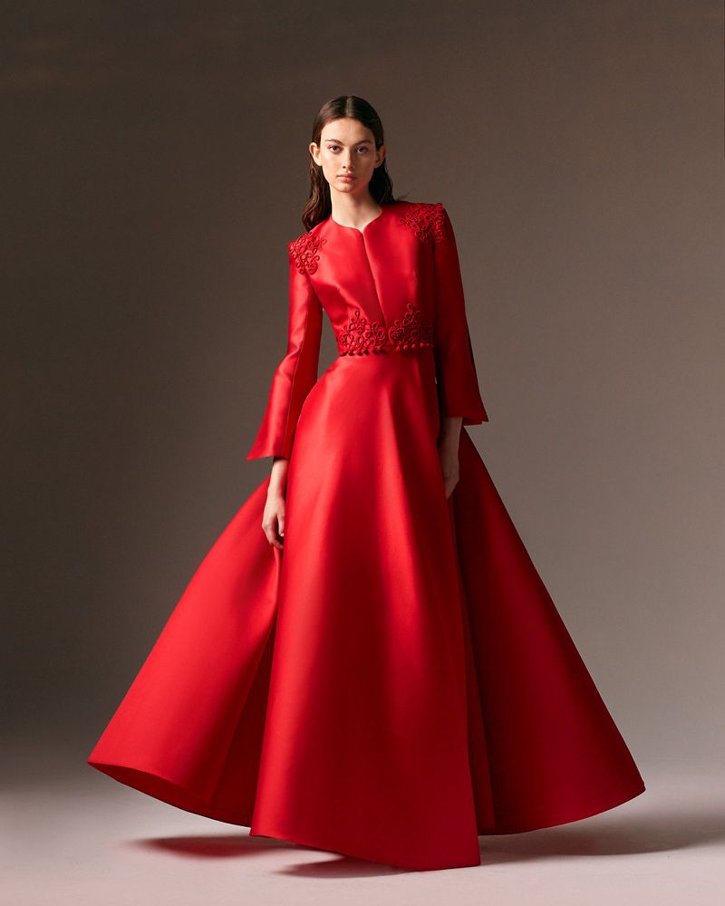 An adult female model poses in a red, floor-length satin gown with decorative embellishments, set against a neutral studio background.