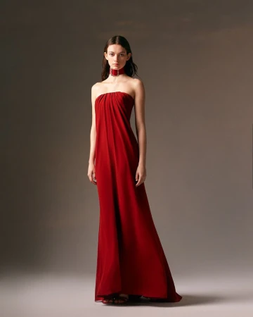 Model Lydia Waldrop wearing a strapless red draped evening gown with a matching choker collar against a neutral studio backdrop.