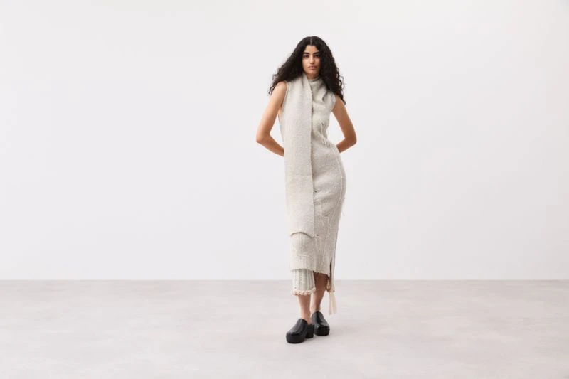 Model Sephora Mosbah posing in a sleeveless cream knit dress and black platform clogs against a bright neutral studio backdrop.