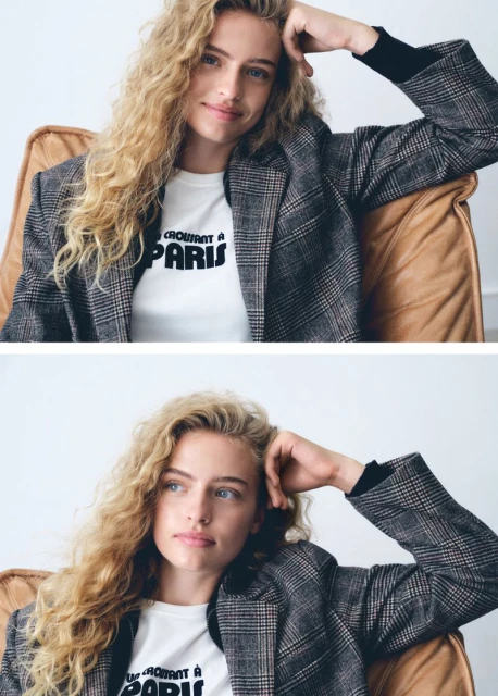 Blonde woman with curly hair poses in an armchair wearing a plaid jacket and 'Croissant a Paris' t-shirt in a portrait shot.
