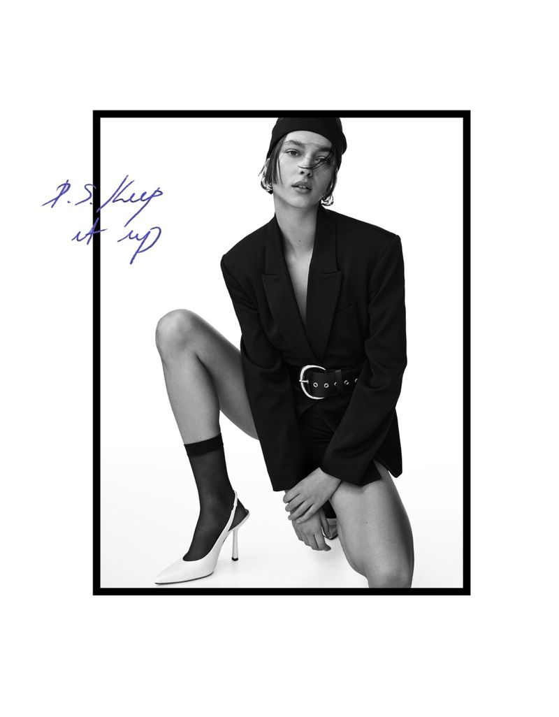 Black and white fashion shot of woman in oversized blazer, beanie, sheer socks, and slingbacks against white with handwriting.