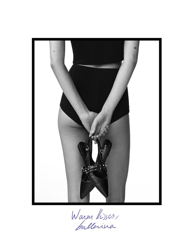 Back view of a woman holding black high heel shoes with studded straps against a white backdrop framed in black and printed with text.