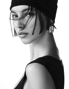 Close-up black and white portrait of a model wearing a black beanie and top against a bright white background