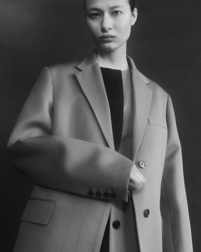 Model Leyla Greiss posing in a tailored oversized blazer and dark crew-neck top against a dark studio background.