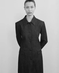 Monochrome portrait of a model standing against a plain white studio background wearing a dark buttoned coat.