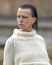Woman with slicked-back hair and smudged eyeliner wearing a thick white knit turtleneck sweater outdoors
