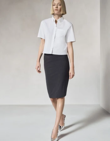 Full-length shot of a blonde woman in a white short-sleeve shirt and dark pencil skirt with metallic flats against a neutral backdrop.