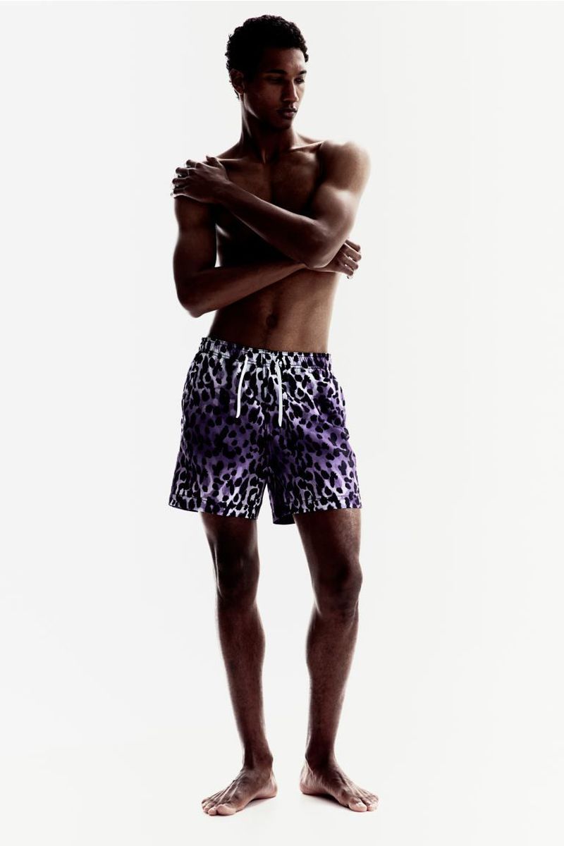 Young adult male model in animal print shorts, arms crossed, posing in a brightly lit photo studio. Fashion and beauty photography.