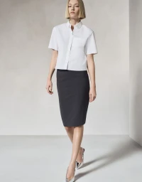 Model wearing a short-sleeve white button-down shirt and dark pencil skirt against a minimalist studio background