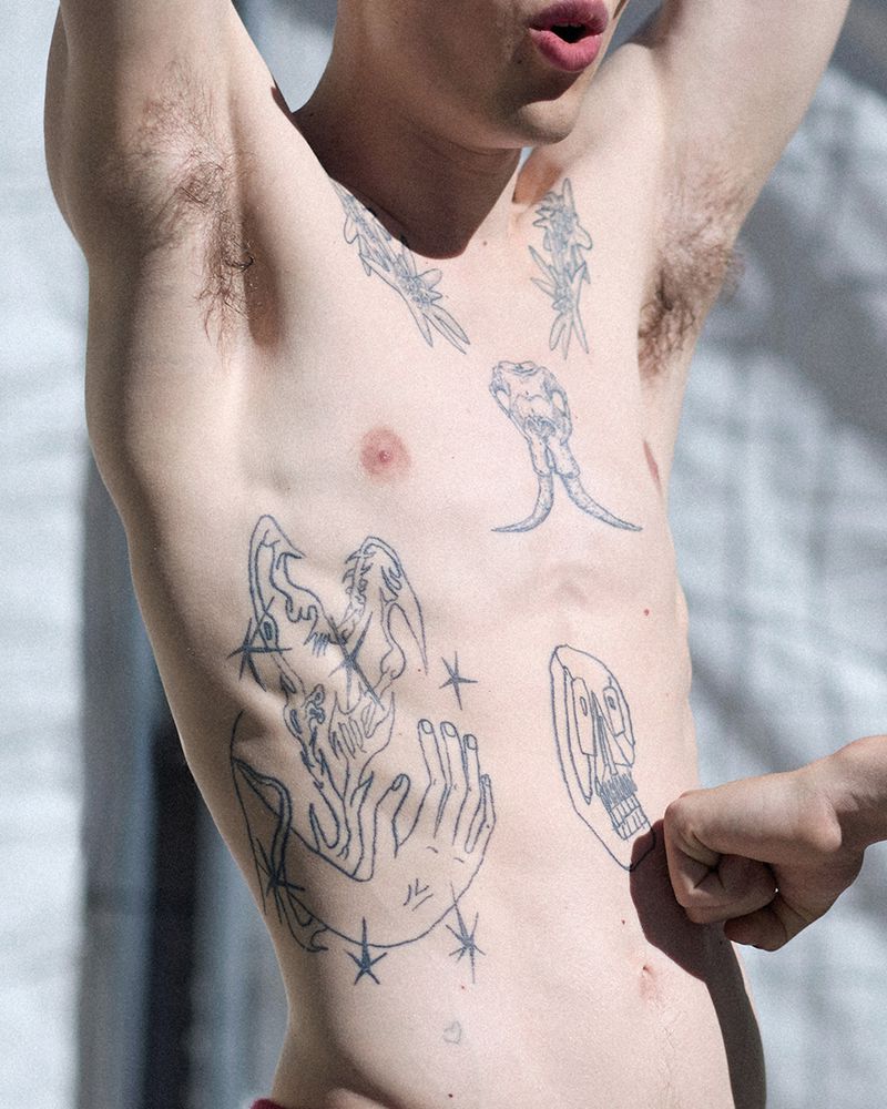 Close-up shot of a shirtless person with multiple tattoos on their torso and arms, raising their arms above their head.
