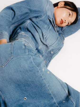 Woman in denim jacket and jeans lies on white backdrop. Cool, casual fashion portrait with blue denim outfit and neutral studio background.