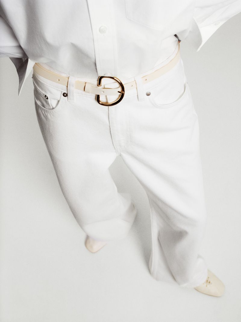 Close-up overhead shot of an adult wearing white denim jeans, a white belt with a gold buckle, and a white button-down shirt.