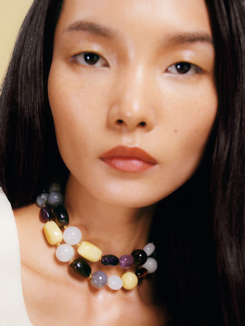 Close-up of an Asian woman with long black hair wearing a beaded necklace with yellow, white, and dark-colored beads.
