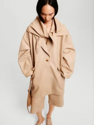 Model Ling Chen wearing an oversized beige leather coat and matching shorts against a plain light studio background.