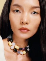Close-up portrait of model Ling Chen wearing a colorful beaded stone necklace against a neutral backdrop for Arket S/S 24.