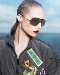 Model Annie Arnander wearing dark shield sunglasses and a grey Ferrari bomber jacket against an ocean horizon.