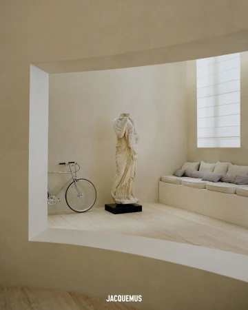 Interior view with a white bicycle, a classical sculpture on a black base, window light, and a low bench with pillows.