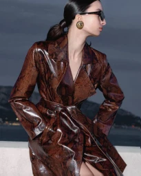 Model in snakeskin print trench coat wearing sunglasses against a coastal dusk background for Nour Hammour Spring Summer 24.