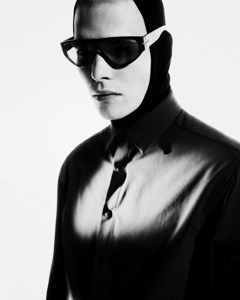 Monochrome portrait of a person wearing futuristic sunglasses and a balaclava-like head covering with a partial view of a collared shirt.