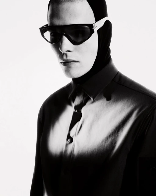 Monochrome portrait of a person wearing futuristic sunglasses and a balaclava-like head covering with a partial view of a collared shirt.