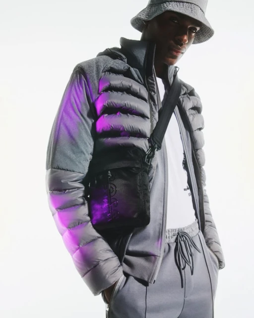 Man in gray puffer jacket and bucket hat with crossbody bag, standing in a bright studio setting. Fashionable and modern style.