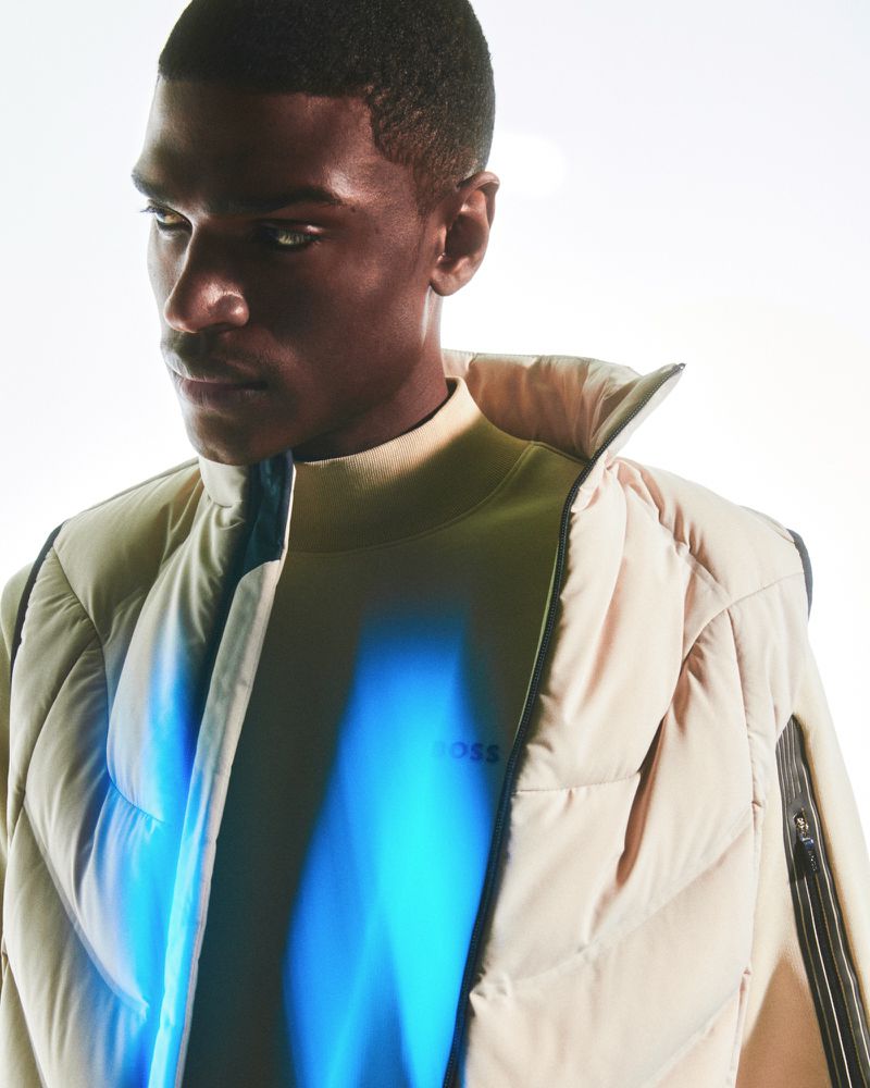 Close-up portrait of an adult Black male model wearing a cream puffer jacket, with a blue light accent and the BOSS logo visible.
