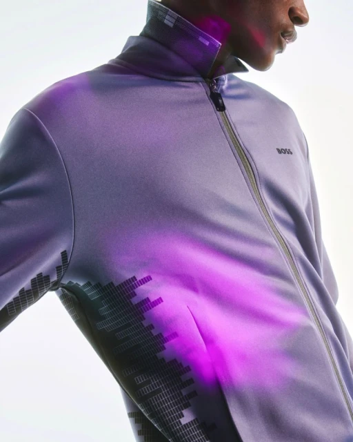 Close-up studio shot of a black male model wearing a light purple zip-up jacket with a geometric print and the 'BOSS' logo.