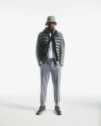 Model Rafael Mayers stands wearing a grey quilted jacket, bucket hat, matching sweatpants, and black sneakers against a white background.