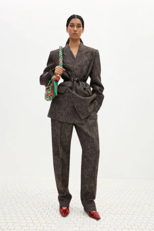 Elegant woman in a tweed suit with shoulder bag and red shoes stands against a white background in a fashion studio shot.
