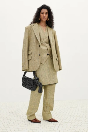 Adult female model wearing an oversized blazer and matching pants, holding a black purse, and posing in a photo studio.