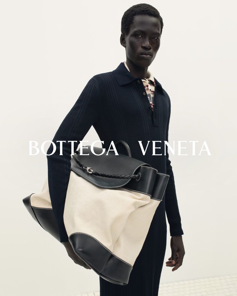 Fashion forward portrait of an adult male model holding a Bottega Veneta bag in a photo studio with white background and studio lighting.