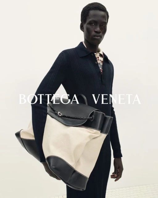 Fashion forward portrait of an adult male model holding a Bottega Veneta bag in a photo studio with white background and studio lighting.