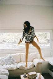Model Nora Attal posing on a white sofa in front of a wide window showing a coastal view for Zara