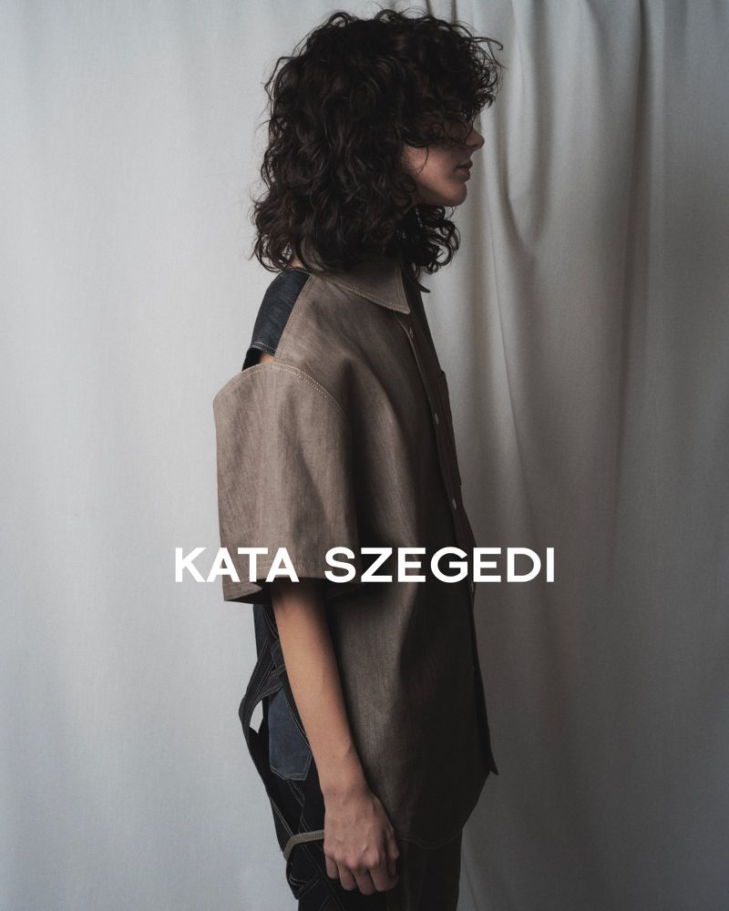 A person with curly hair in a studio setting wears a short-sleeved top. The image features a minimalist aesthetic and neutral color palette.