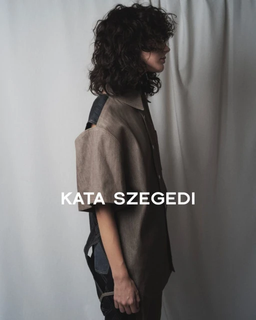A person with curly hair in a studio setting wears a short-sleeved top. The image features a minimalist aesthetic and neutral color palette.