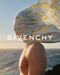 Model with a lemon-patterned silk scarf billowing over their head against an ocean horizon at sunset.