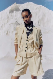 Model wearing a cream suit and patterned scarf against a bright white mountainous terrain background