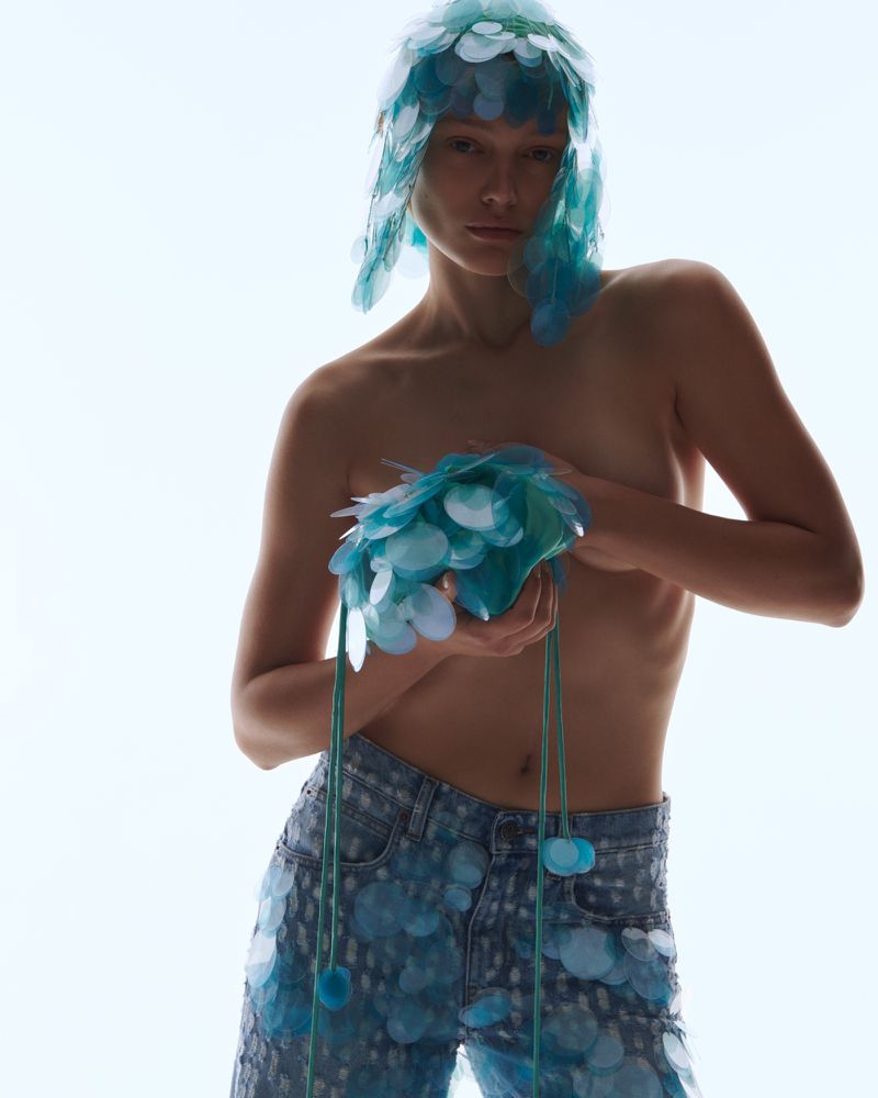 Fashion shot of a model wearing blue jeans and a matching paillette headdress and top. The model poses in a bright, even light.