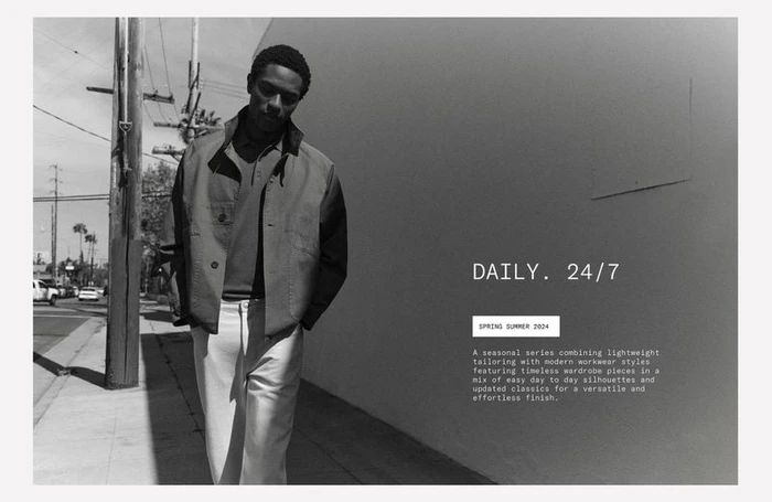 Black and white portrait of a model walking on a city sidewalk past a blank wall for the Zara Daily 24/7 campaign.