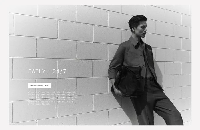 Monochrome fashion portrait of a male model leaning against a white brick wall holding a dark bag for Zara.