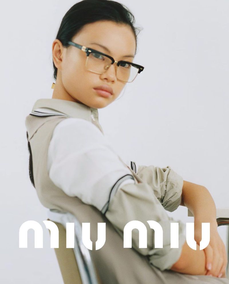 Portrait of an Asian woman wearing glasses and a collared shirt with a neutral vest, posing in front of a plain background.