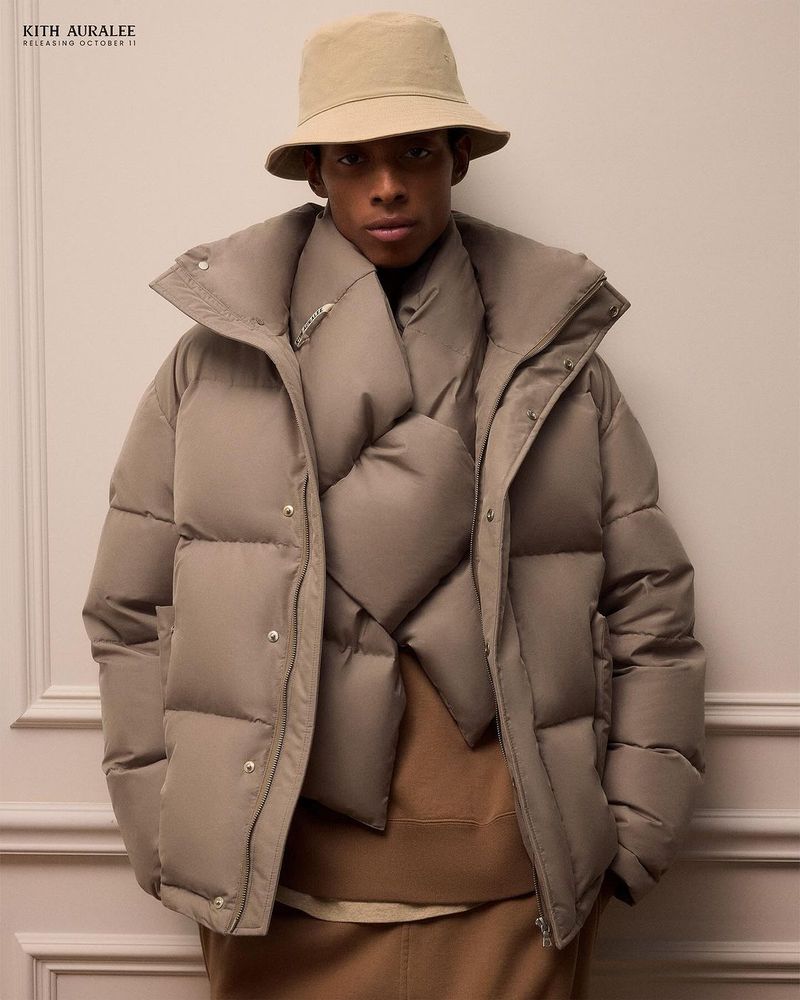 Model wearing a neutral padded puffer jacket and bucket hat against a plain wall.