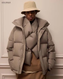 Model wearing a neutral padded puffer jacket and bucket hat against a plain wall.