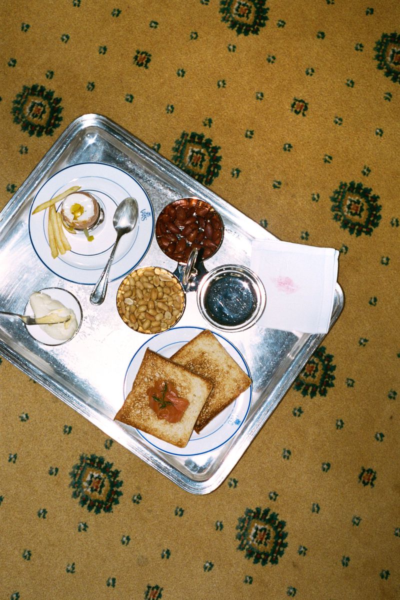 Overhead shot of a silver tray with assorted breakfast items like toast, egg, beans, and jam, resting on a patterned carpet.