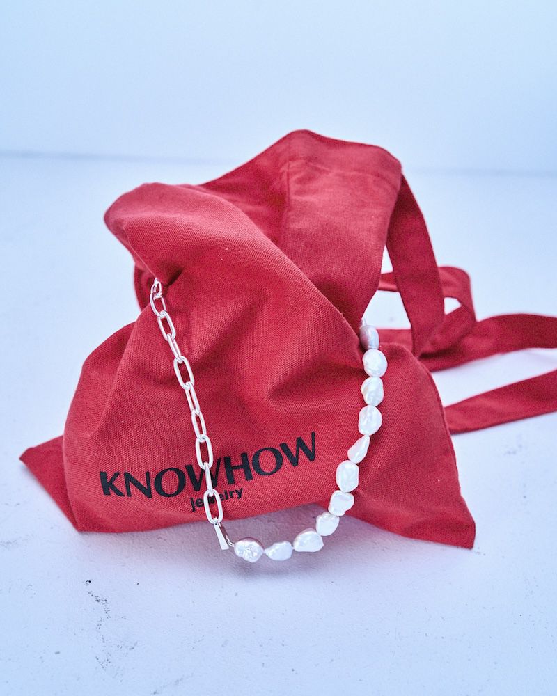 Elegant pearl necklace with a silver chain is draped across a vibrant red drawstring pouch, set against a soft, neutral background.