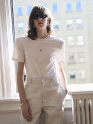 Model wearing dark sunglasses, layered pearl necklaces, a white t-shirt, and trousers by a window